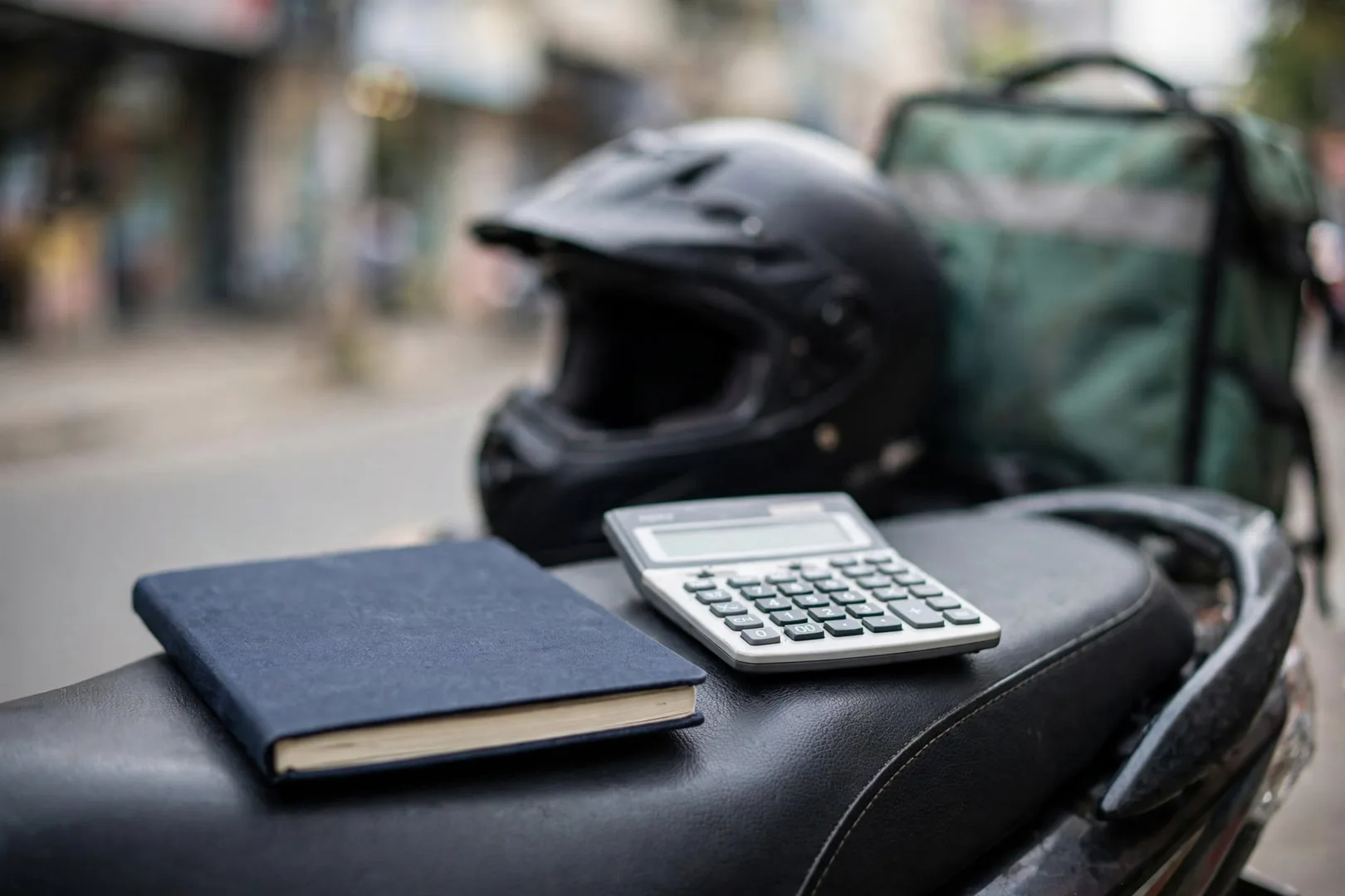 Caderno de anotações e calculadora sobre o banco da motocicleta de entregas para o cálculo do custo por quilômetro